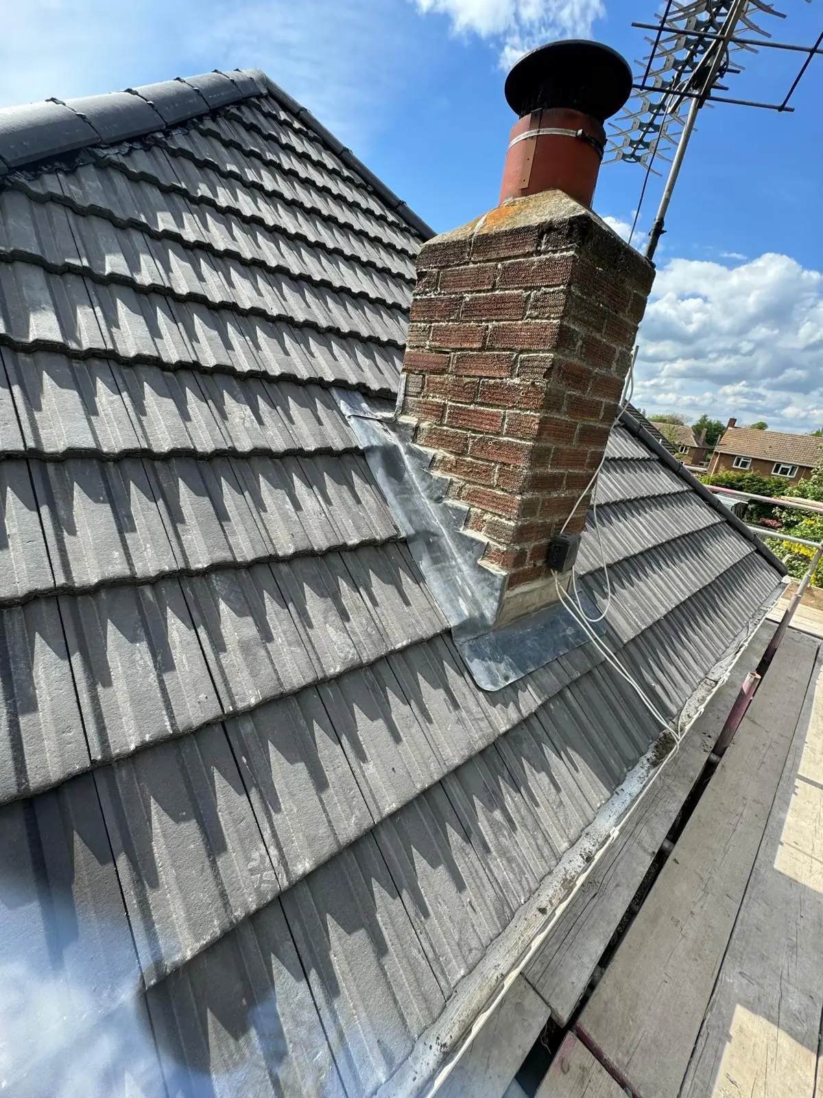 A brick chimney with new lead flashing on a finished grey tiled roof