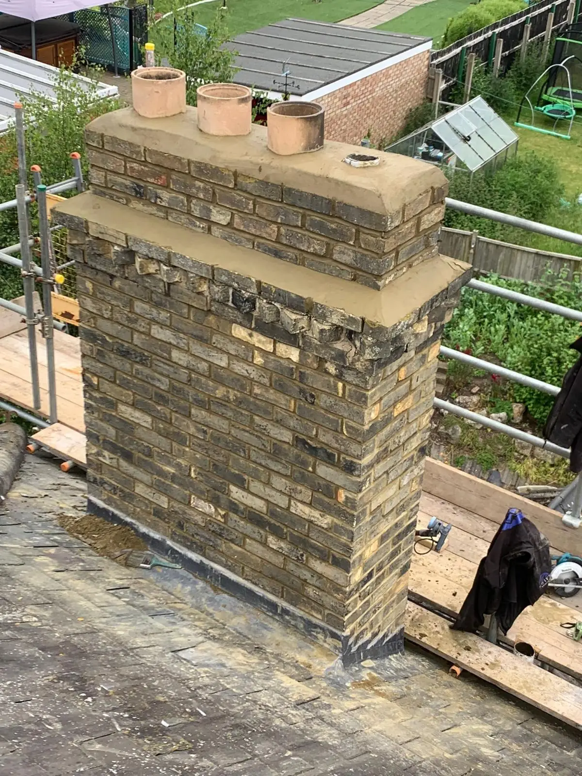 A rebuilt brick chimney stack with new pots fitted, scaffold around it