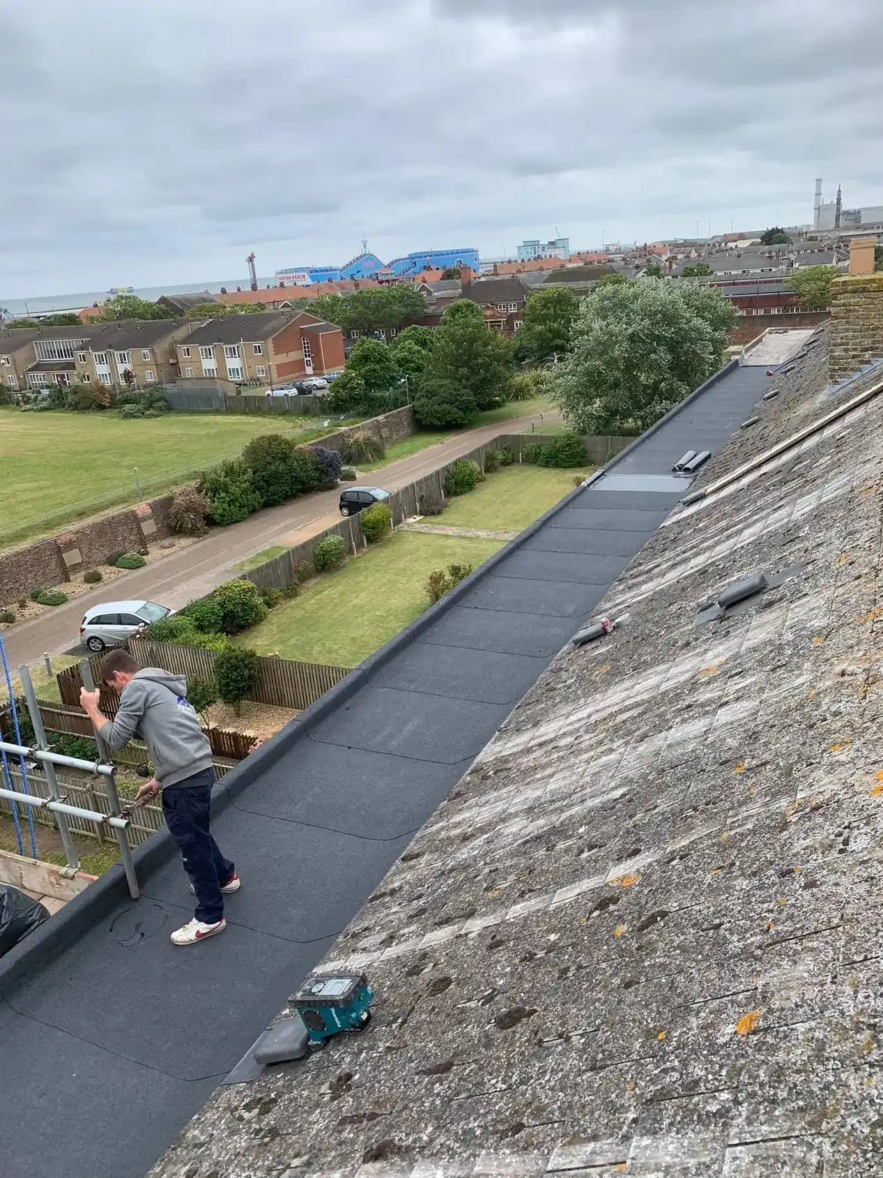 A large commercial flat roof completed above a town, with the roofer checking the finished surface