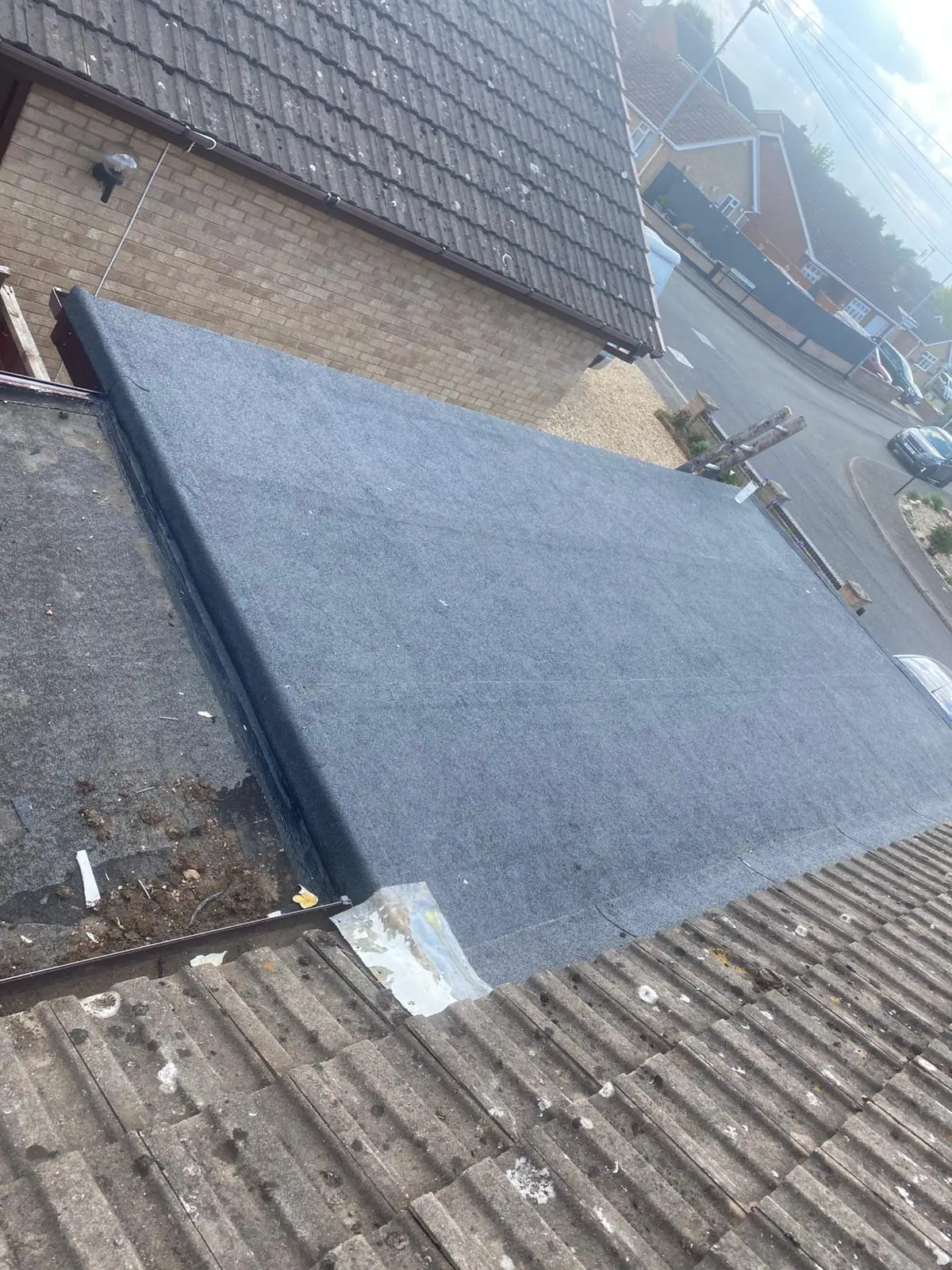 A newly laid dark flat roof beside a pantile roof and chimney stack