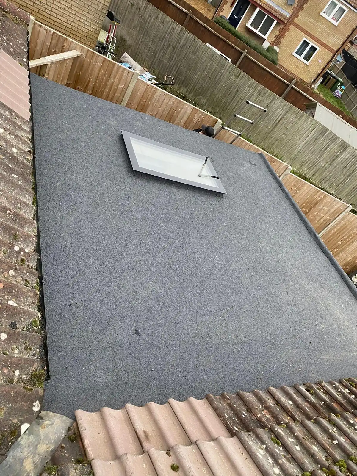 A new grey flat roof with a rooflight fitted, garden fence beyond