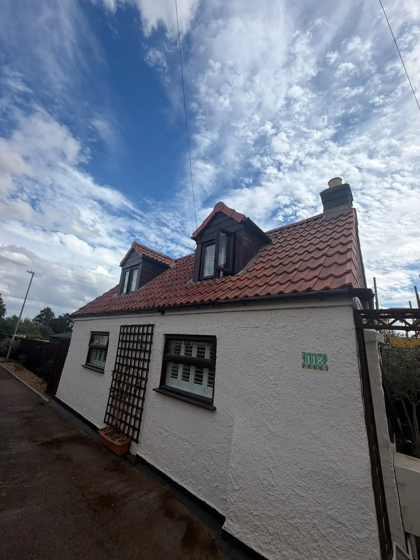 A white rendered cottage with a newly re-tiled red clay pantile roof and dormer window
