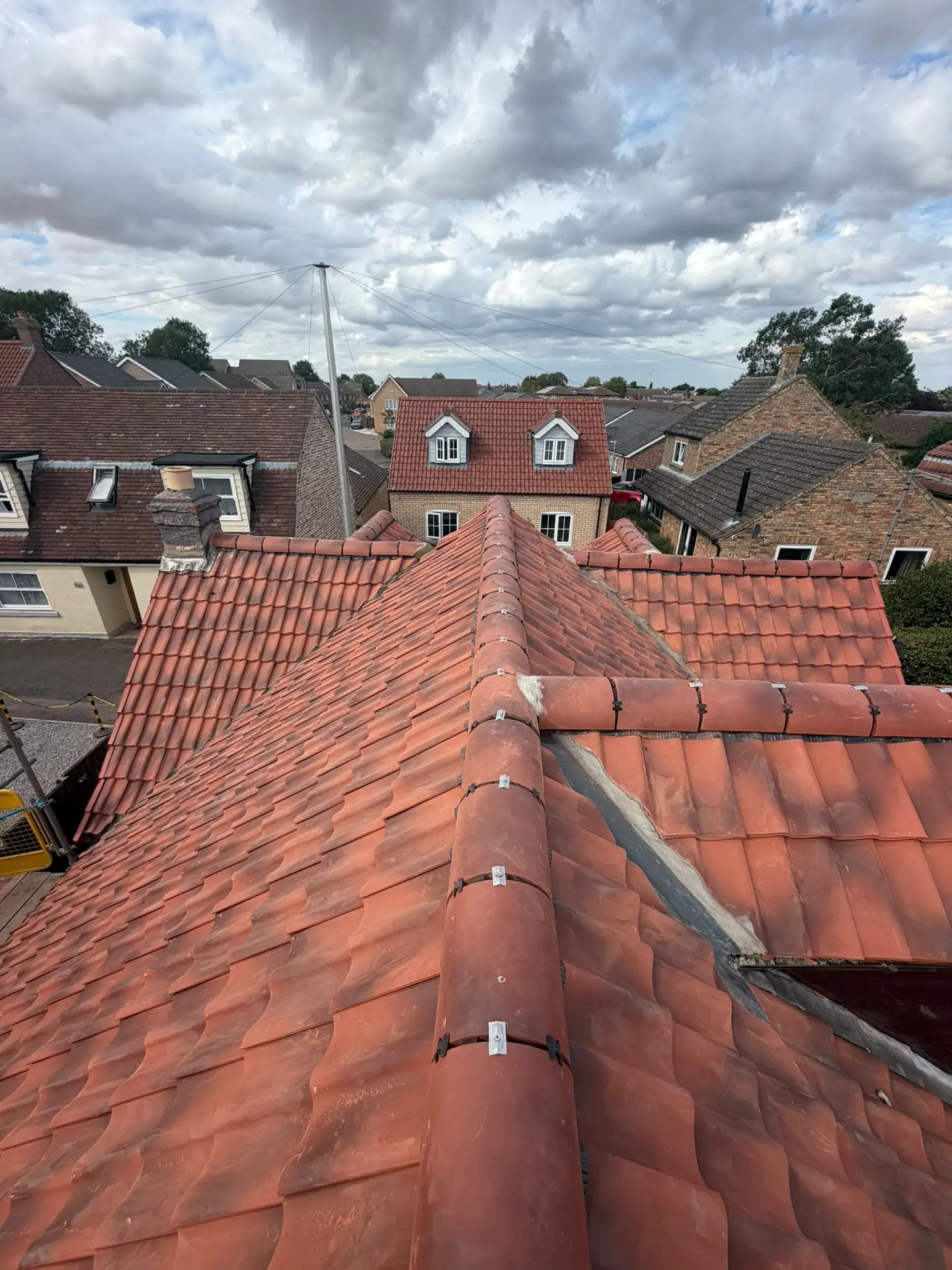 A red clay pantile roof with a new ridge line, rooftops behind