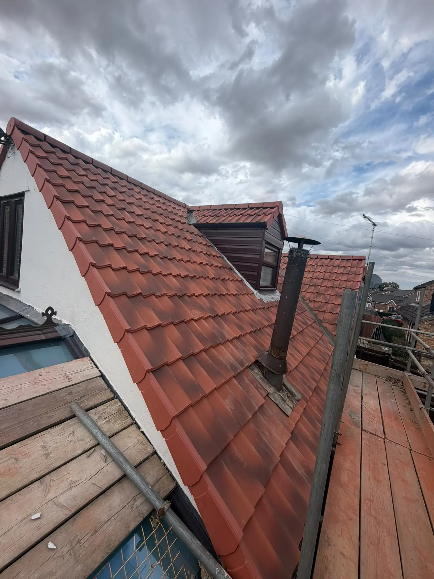 A red pantile roof with the valley and dormer finished, scaffold boards alongside
