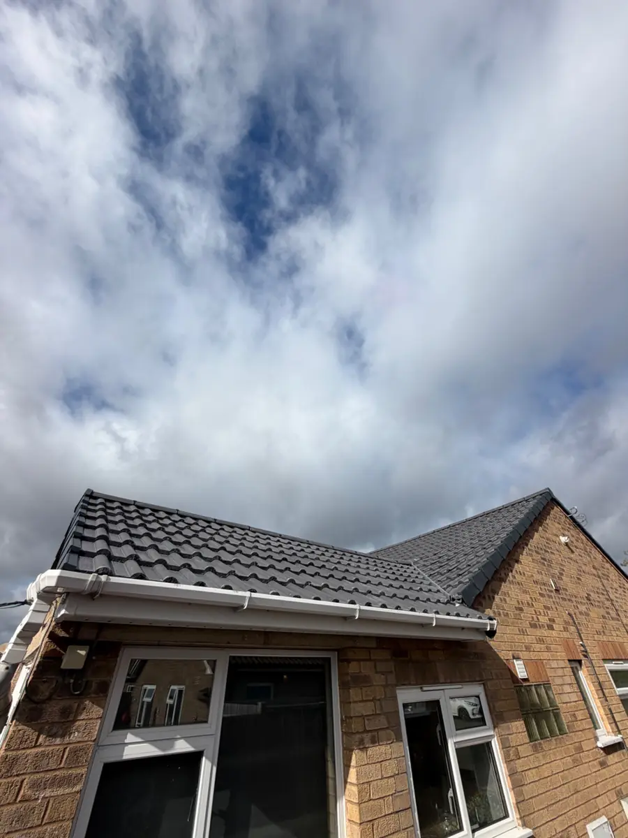New dark grey tiles above white fascia and guttering on a brick bungalow