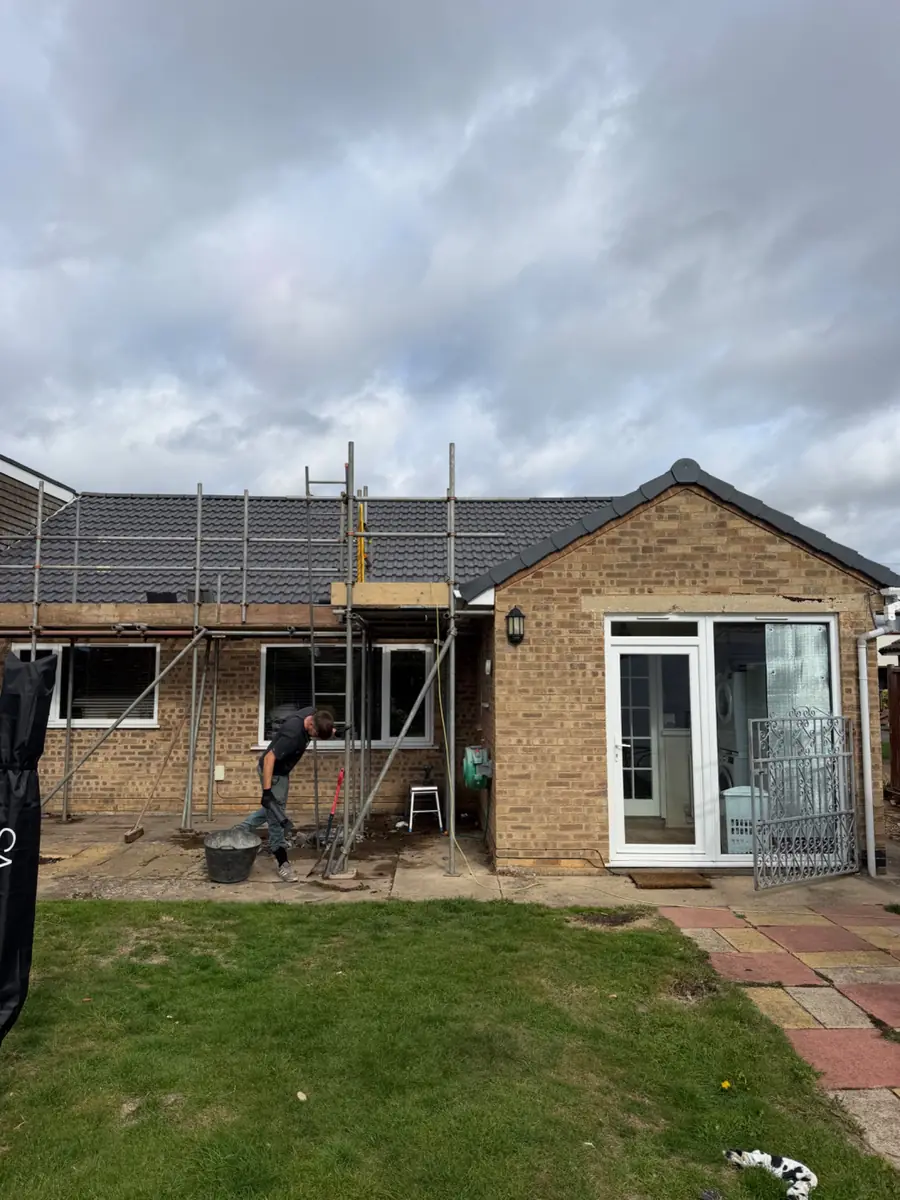 The rear of a brick bungalow with scaffold along the roof and a Swift Roofing roofer working below