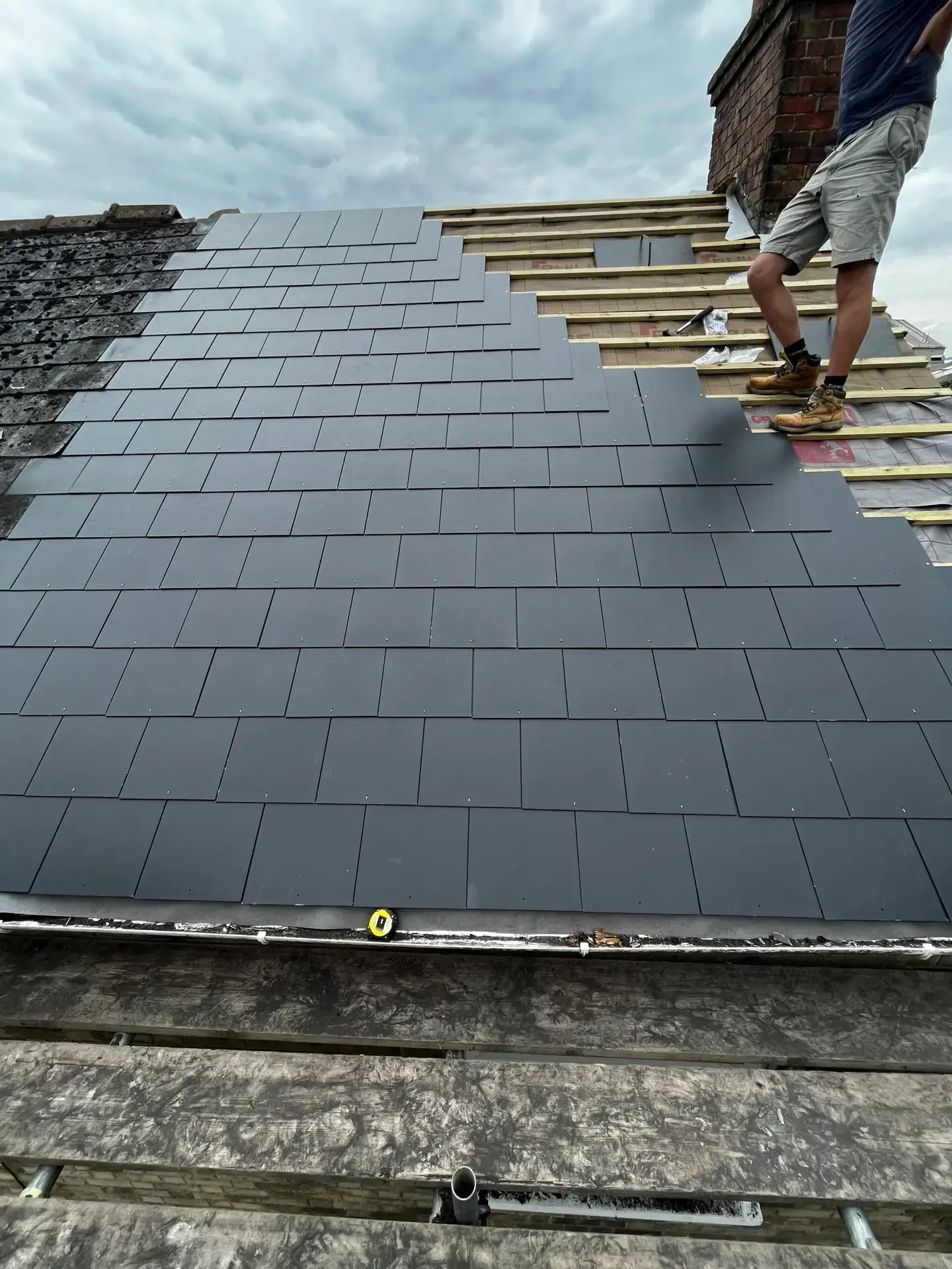 Dark flat slate tiles being laid over new battens on a pitched roof
