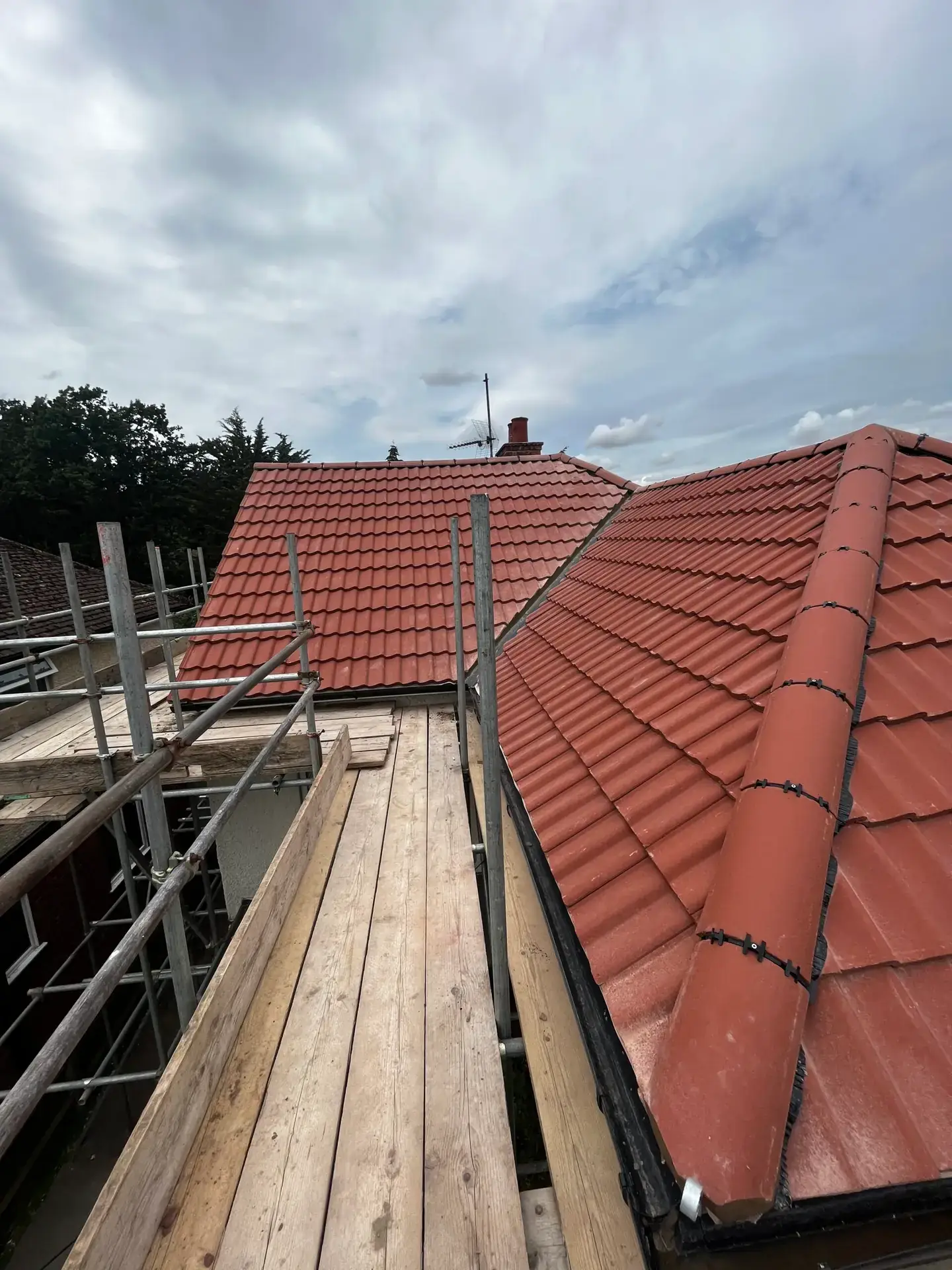 A red pantile roof part way through replacement, with scaffold boards running along the eaves