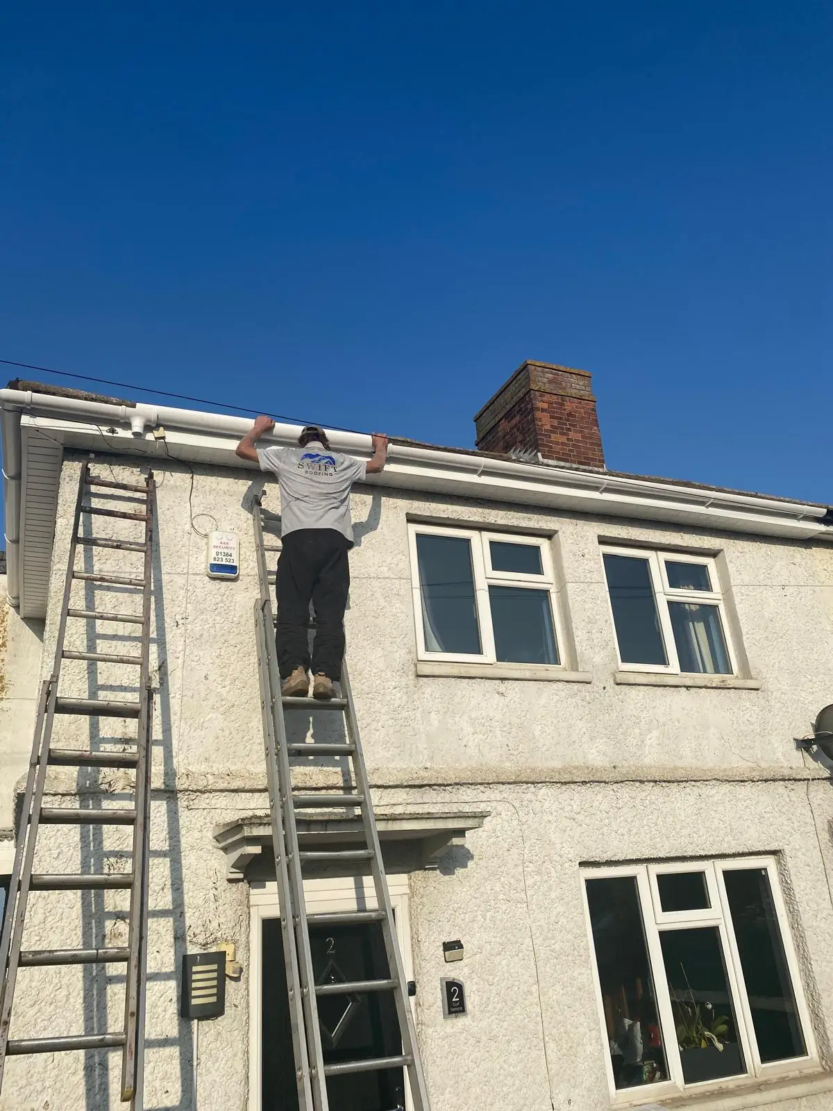 A Swift Roofing roofer working at height from ladders on a rendered house