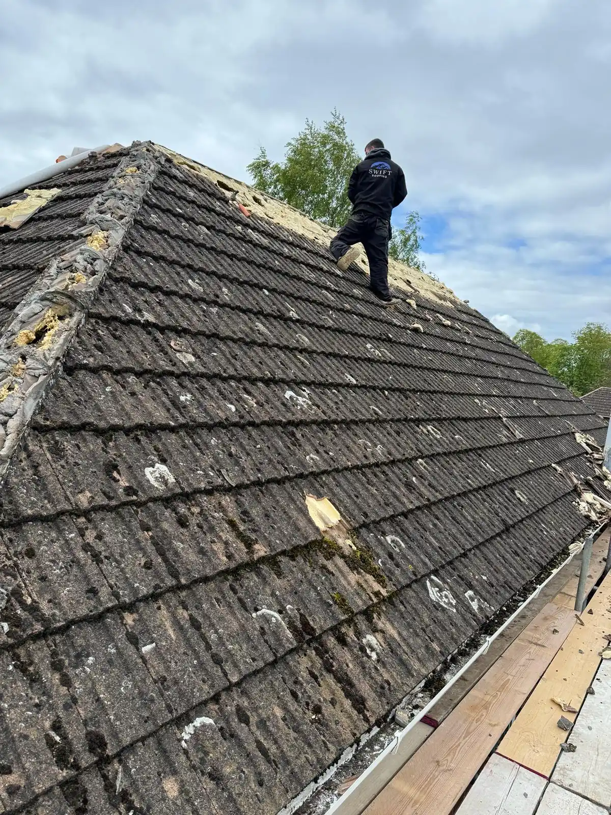 A roofer stripping the old tiles from a hip roof during a re-roof