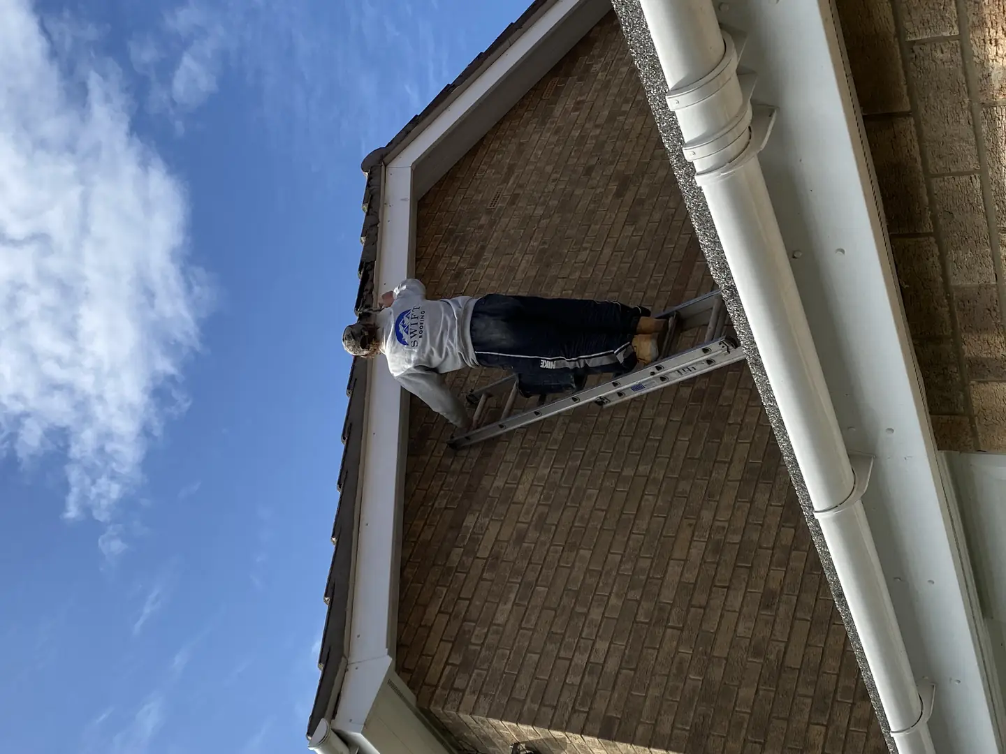 A Swift Roofing fitter installing new white uPVC guttering from a ladder