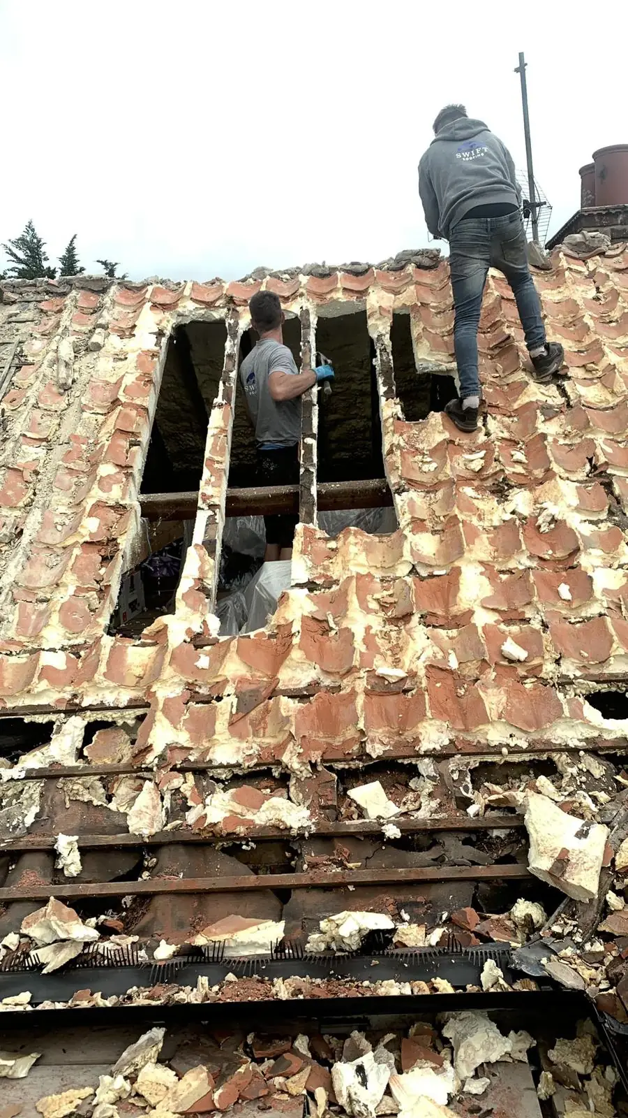 A Swift Roofing roofer stripping a spray foam insulated roof, foam broken away from the battens
