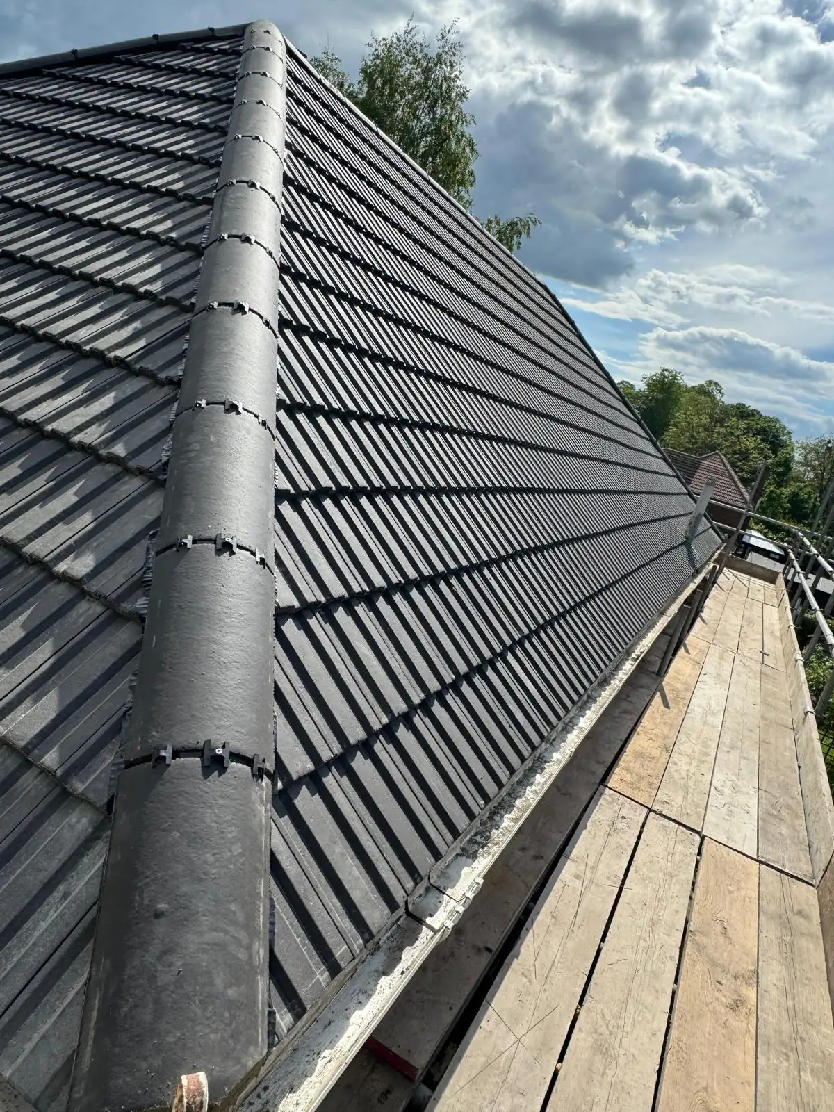 A finished dark grey tiled roof with new ridge tiles and a flue