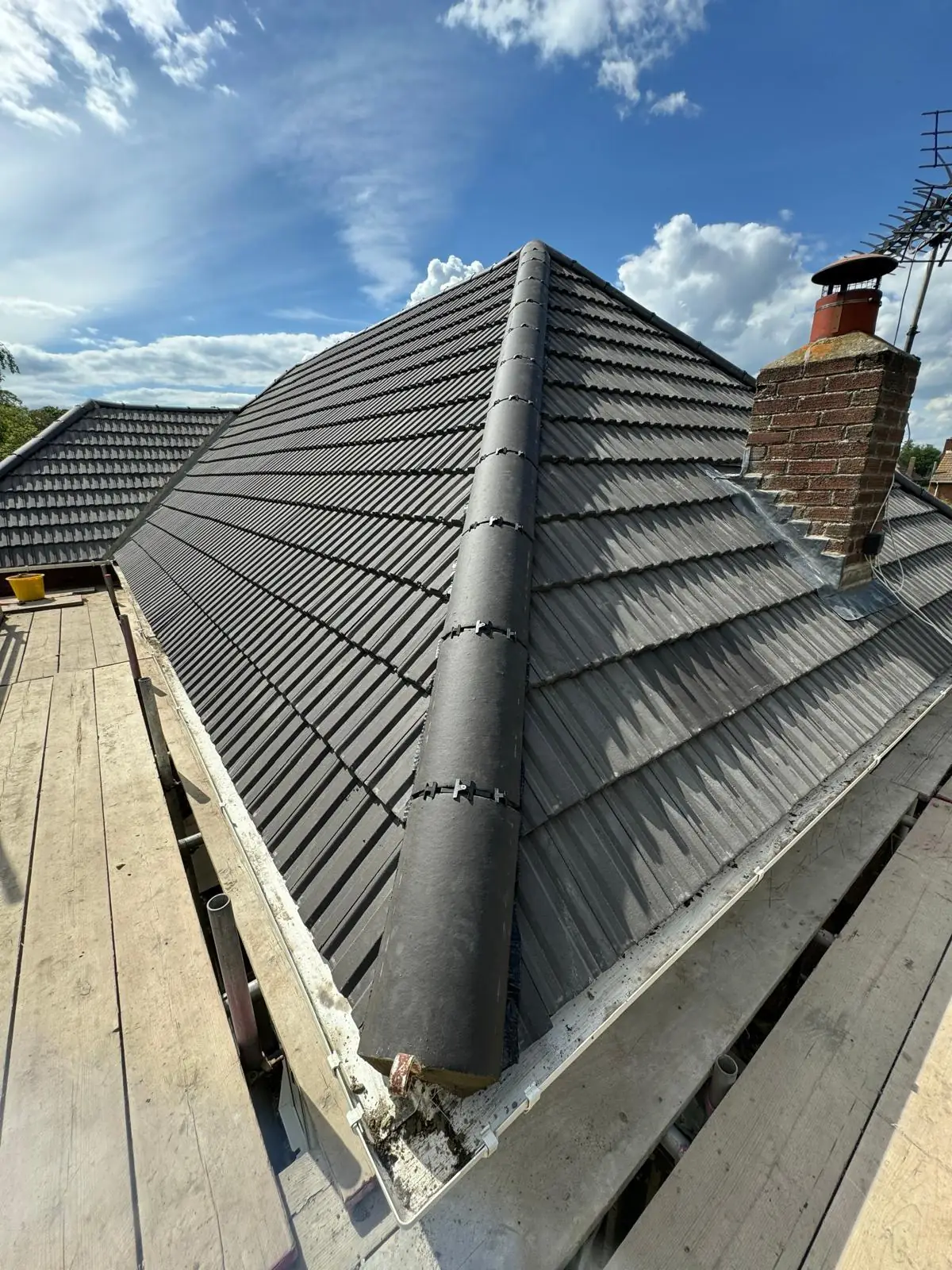 A completed grey tiled hip roof with the chimney stack rebuilt alongside