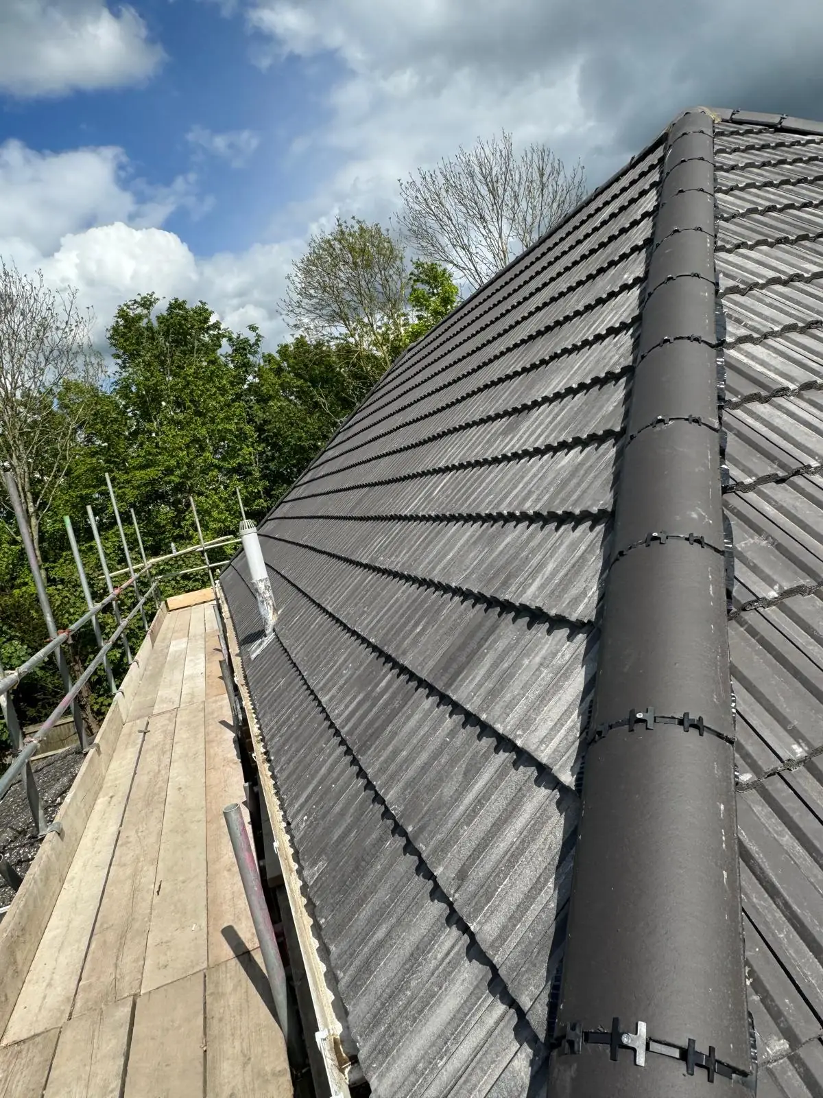 A finished grey tiled hip roof with the scaffold still standing