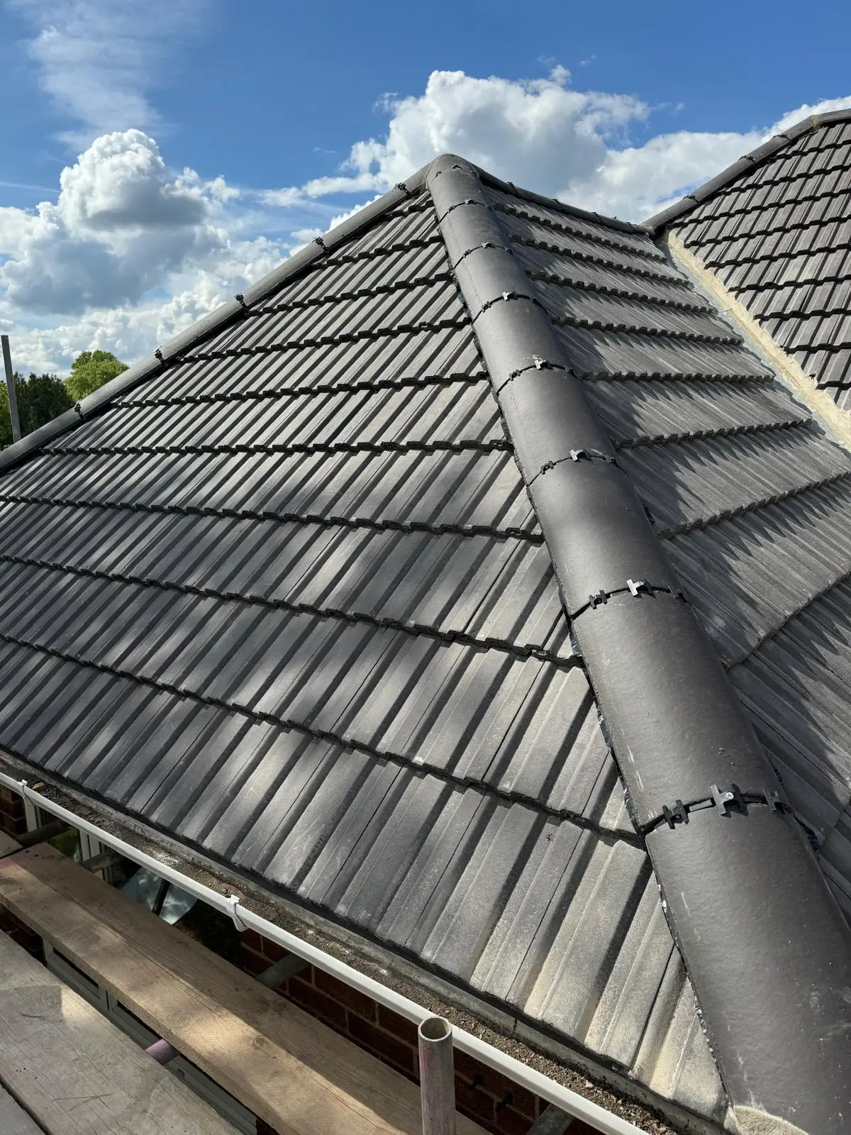 A wide view of a finished grey tiled hip roof against blue sky