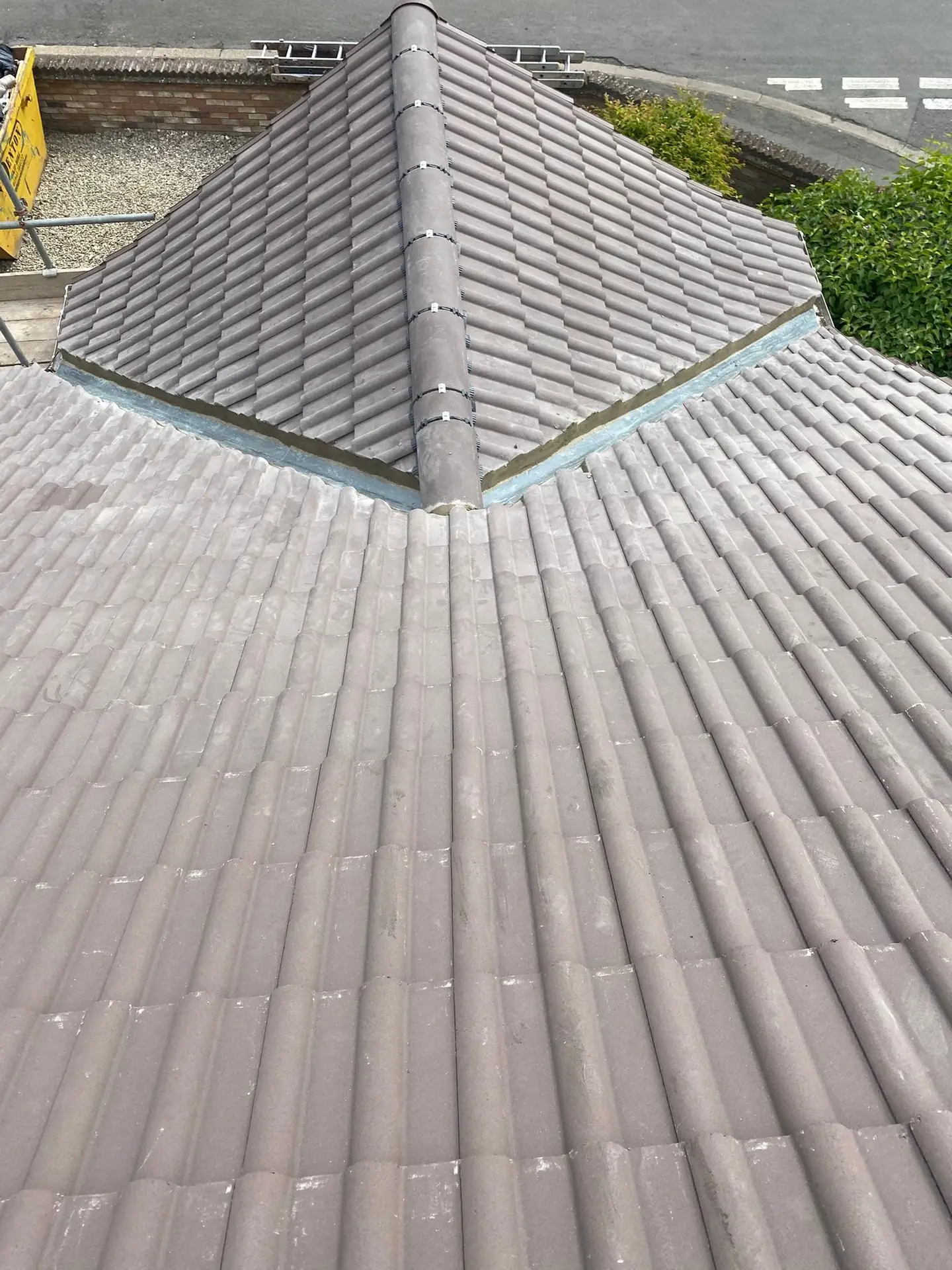 A finished grey tiled pyramid hip roof viewed from the scaffold